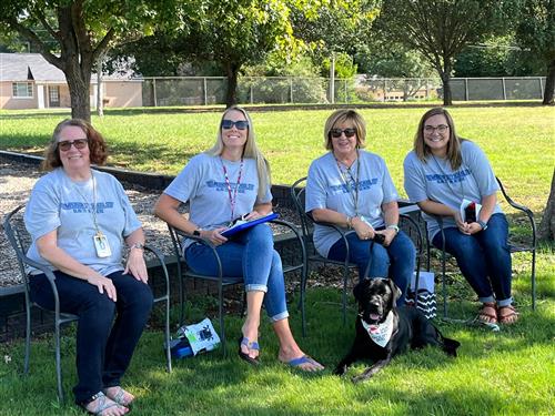 Teachers seated in shade with Barnie the facility dog at Madison Elementary